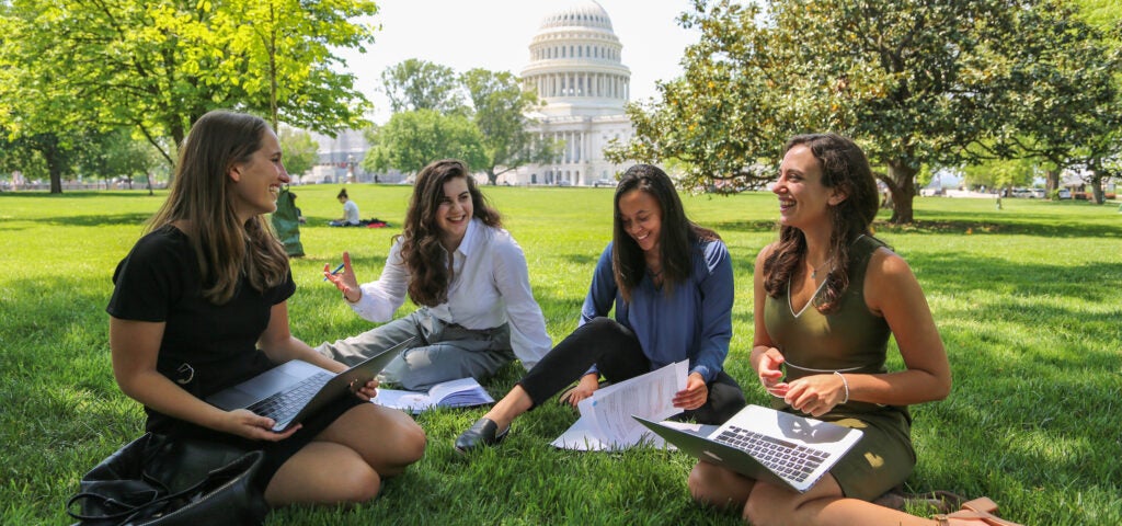 four students sitting on the lawn in front of the US Capitol Building, studying and talking