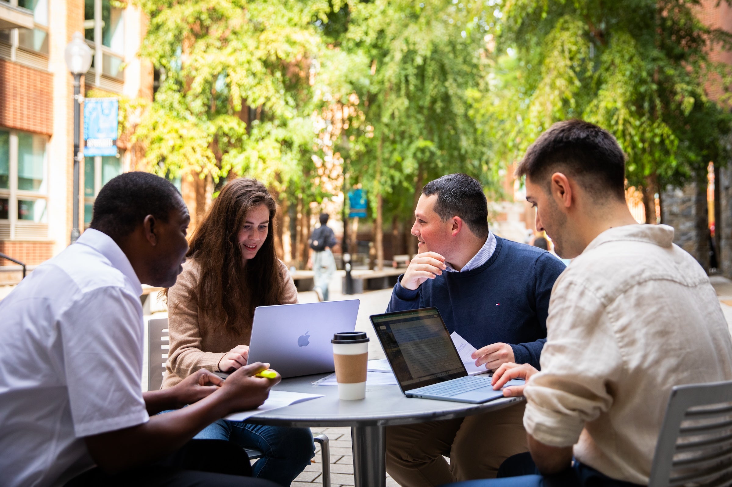 Four students studying together at a table outside with laptops