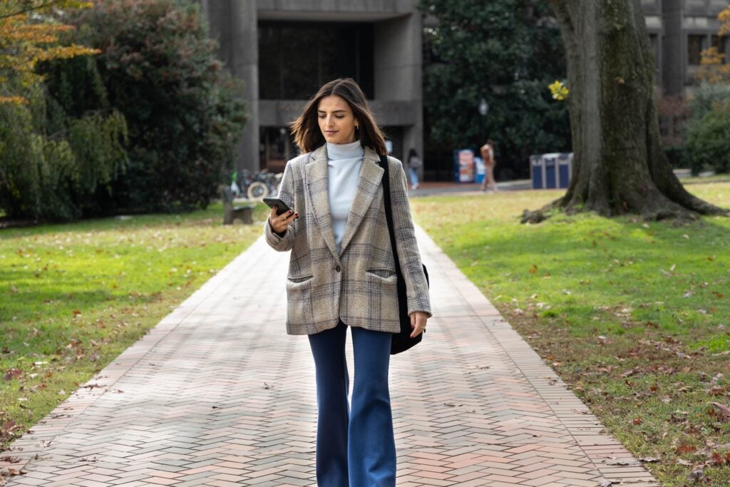 student in a plaid blazer and jeans walking to class looking at a phone