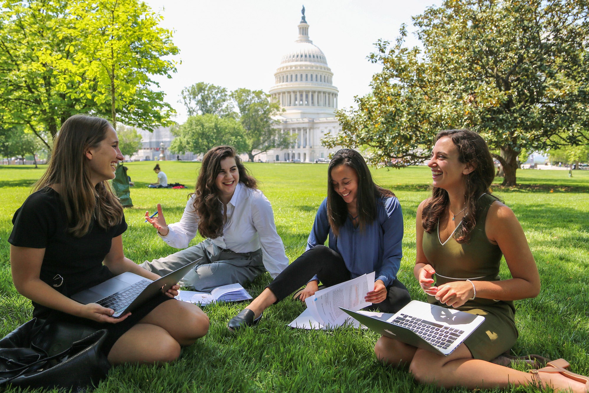 Four students sitting on the lawn in front of the Capitol Dome