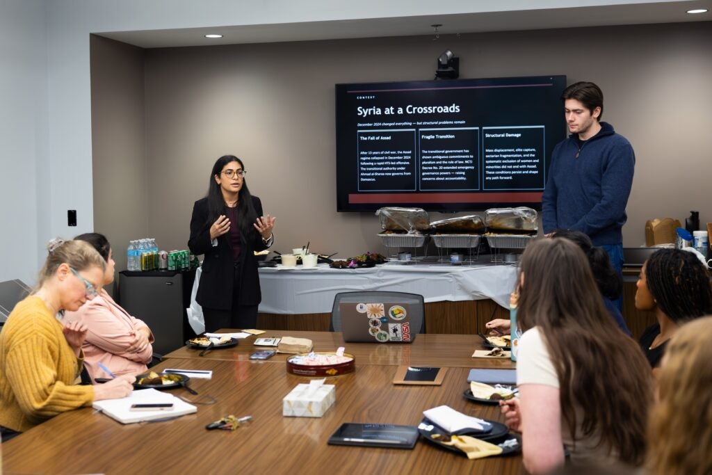 May and Antoine stand at the front of a room and give a presentation about their conflict resolution training practicum experience